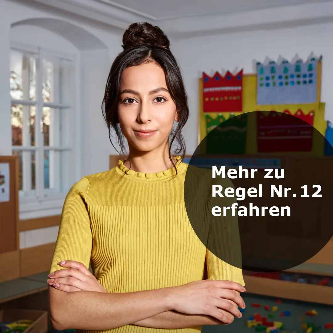 Frau mit hochgestecktem Haar in gelbem Pullover steht mit verschränkten Armen in einem Kindergartenraum.