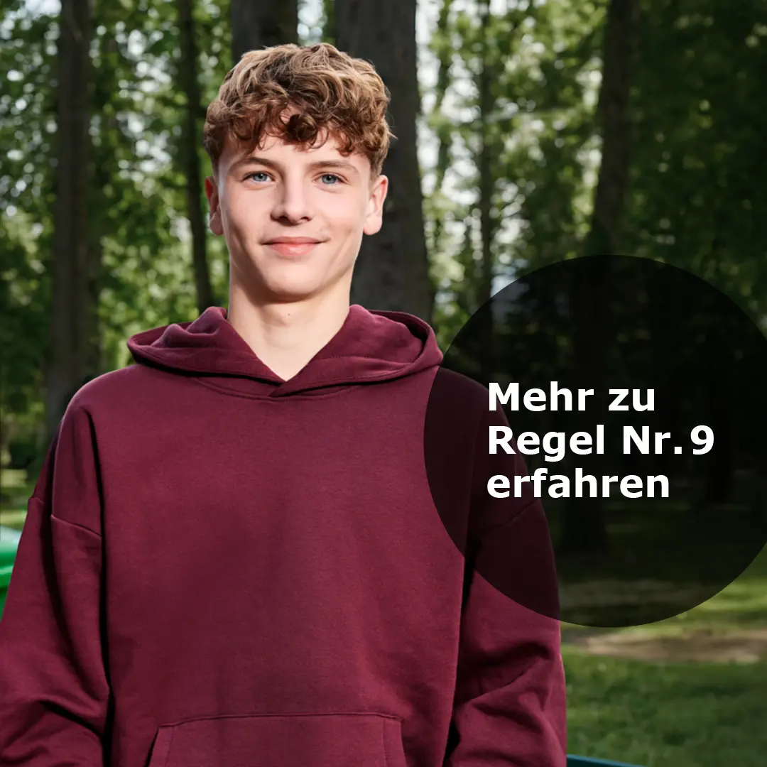 Junger Mann in bordeauxrotem Kapuzenpullover steht im Park mit Bäumen im Hintergrund und Text